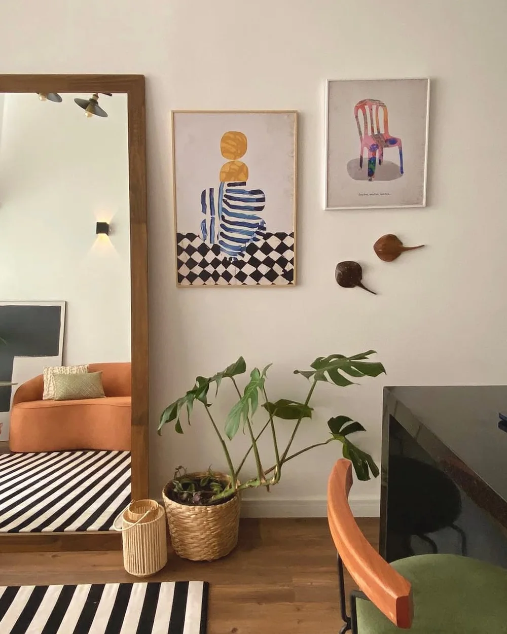 Canto de estar com sofá laranja, arte na parede e plantas